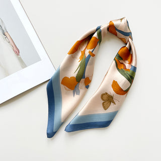 Elegant Iris Melody silk scarf with orange flowers and butterfly design on cream background with blue border, styled in bandana form