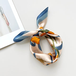Blue Orange Iris Melody silk bandana scarf tied in a knot, featuring peach background with vibrant blue borders, orange iris flowers and green stems