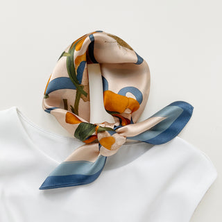Blue Orange Iris Melody silk bandana scarf with floral pattern, tied in a knot and displayed on white fabric, showing luxurious sheen and vibrant colors