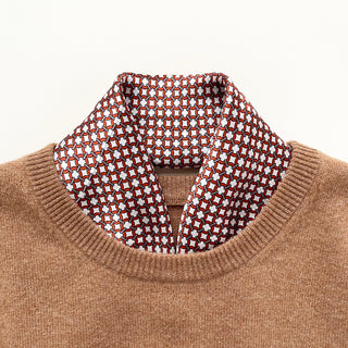Red silk scarf with navy and white geometric lattice pattern styled as a neckerchief with a camel-colored sweater, showcasing the luxurious texture