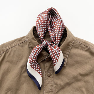 Red and white lattice silk scarf with navy blue trim tied elegantly around a tan shirt collar, displaying the modern geometric pattern