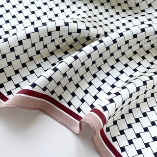 Luxurious silk scarf featuring white and navy geometric squares pattern with elegant burgundy and pink border trim, showcasing silky texture and soft drape