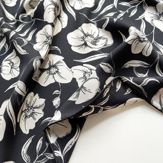 Close-up of a women’s 65cm silk square scarf with off white poppy blossom floral print in black background, double-sided silk twill and hand-rolled hems by LuluLane