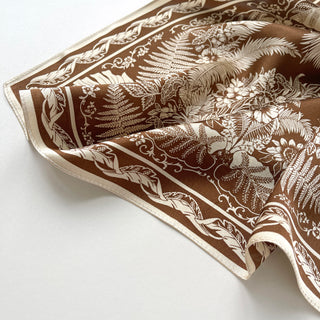 Bronze silk bandana scarf featuring intricate cream fern and monstera leaf patterns with decorative border and elegant botanical design