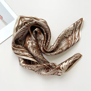 Bronze silk bandana scarf with elegant cream botanical pattern featuring fern and monstera leaves, artfully draped to showcase luxurious sheen and square design.