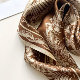 Luxurious bronze silk bandana scarf with elegant cream botanical pattern featuring ferns, flowers and monstera leaves on a sleek shimmering fabric
