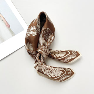 Bronze silk bandana scarf with cream botanical pattern featuring fern and monstera leaves, elegantly tied and displayed on white surface