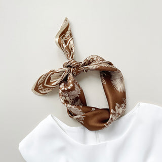 Bronze silk bandana scarf with elegant white fern and floral pattern, tied in a stylish knot atop a white garment against light background.