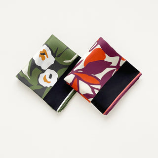 Two folded silk bandanas with floral patterns - one in burgundy purple with white blooms, one in forest green with matching design, both featuring hand-rolled edges