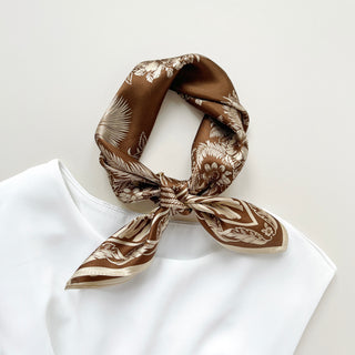 Bronze silk bandana scarf with cream fern and floral pattern, elegantly tied and displayed on a white fabric against neutral background