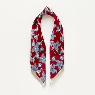 Women's silk bandana scarf by LuluLane with vibrant red background featuring blue floral botanical pattern and cream-colored border.