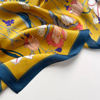 Mustard yellow silk scarf with floral and butterfly print featuring pink, white, and purple blooms with navy blue border on luxurious shimmering fabric