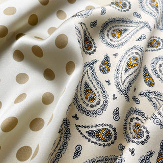 Close-up of beige silk scarf by LuluLane with intricate black paisley pattern on one side, solid cream color on the other, featuring elegant brown border trim