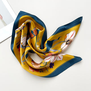 Mustard yellow silk scarf with navy blue border, featuring vintage floral and butterfly print. Square bandana elegantly draped to showcase glossy fabric texture.