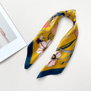 Mustard yellow silk bandana scarf with floral and butterfly print featuring white flowers and navy blue border, arranged in a loop on white surface