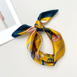 Mustard yellow silk bandana scarf with navy border, elegantly tied, featuring butterfly and floral pattern in orange, blue and cream tones.