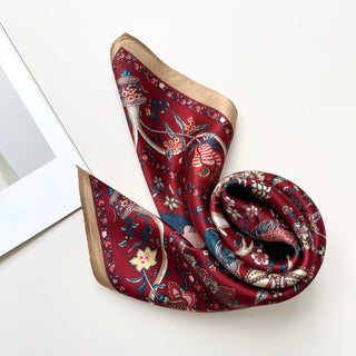 Rich red silk scarf with vintage floral pattern featuring ornate botanical designs in blue, gold and white with elegant beige border, displayed in graceful folds