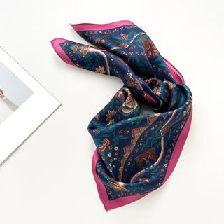 Elegant blue silk scarf with vintage floral pattern, pink border, and decorative botanical designs, artfully draped to showcase its luxurious sheen