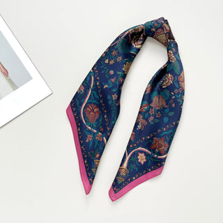 Blue silk scarf with vintage floral pattern featuring pink and gold botanical designs, pink border, and elegant sheen, displayed in a folded position.
