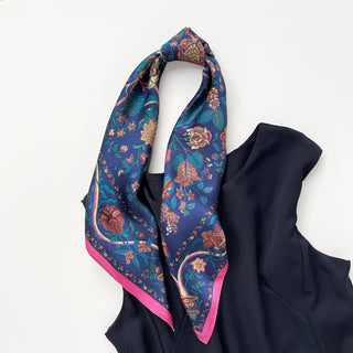Navy blue silk scarf with vintage floral pattern featuring red and gold flowers, teal leaves, and pink border, draped over black fabric