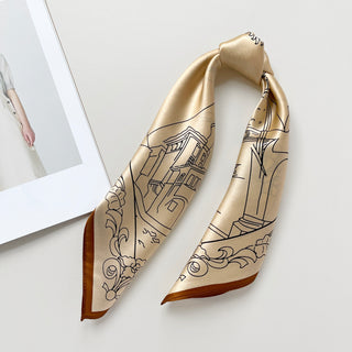 Beige silk scarf with black line art depicting cityscape architecture, folded to display shimmering fabric and brown border, on neutral background.