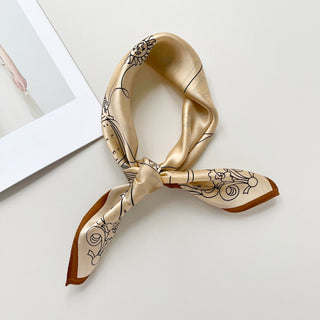 beige silk bandana scarf with black line art featuring sun motifs, elegantly tied and displayed on white surface with brown trim edge