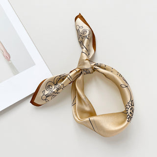 beige silk bandana scarf with brown border and abstract line art design, tied in a knot showcasing its luxurious sheen