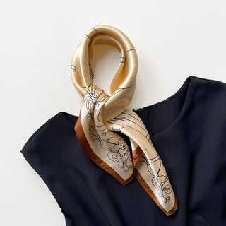 beige silk bandana scarf with elegant black line art designs and copper-brown border, elegantly draped on navy blue fabric