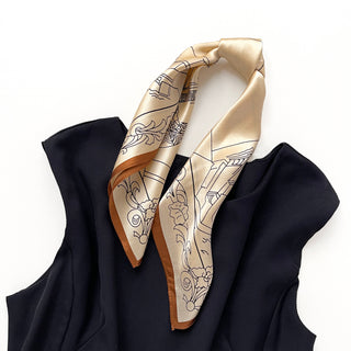 Beige silk bandana scarf with black architectural line drawings and copper border, elegantly draped on a navy garment