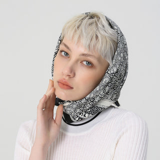 Silk scarf with black and white intricate pattern worn as head covering, styled with white sweater, showcasing elegant draping and luxurious texture