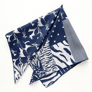 Navy and white silk scarf featuring mixed patterns of floral motifs, polka dots, and animal prints with hand-rolled edges in square bandana style