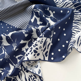 Navy and white silk scarf featuring mixed patterns of florals, polka dots, stripes, and leopard print with elegant hand-rolled edges