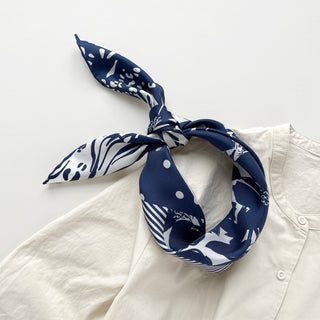 Navy silk bandana scarf with white patterns including polka dots and animal prints, tied stylishly on a cream blouse collar