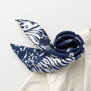 Navy and white silk scarf with mixed animal print and floral motifs, elegantly rolled to display its luxurious texture and hand-rolled edges.