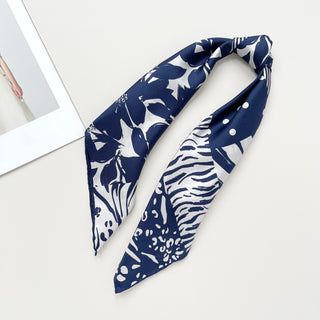 Navy and white silk scarf featuring mixed animal prints and floral patterns with polka dots, displayed in a stylish fold with hand-rolled edges