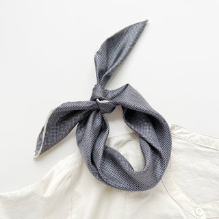 Black and white silk bandana with elegant grid and dot pattern tied in a decorative knot against white collar, showing fine hand-rolled edges