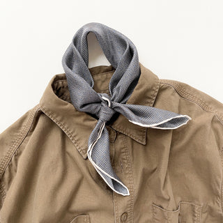 Black and white silk bandana with grid and dot pattern, elegantly tied around the collar of a tan jacket, showing its versatile styling