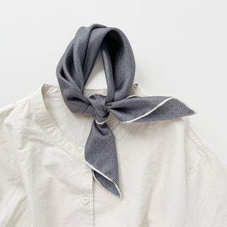 Silk scarf with black and white grid dot pattern tied around collar of cream shirt, featuring elegant white border trim
