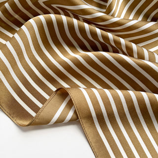 Luxurious silk bandana scarf with golden bronze and white striped pattern, elegantly draped showing its smooth texture and silky finish.