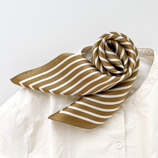 Luxurious silk bandana scarf featuring bronze and white striped pattern, elegantly tied on white shirt collar with geometric design.