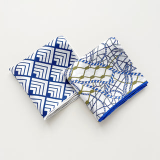 Two folded silk bandanas with blue and white geometric patterns - one with angular maze design, one with nautical rope pattern and gold accents