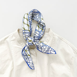 Silk bandana with white background, blue rope pattern and gold accents, tied elegantly around collar of cream shirt