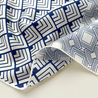 Close-up of silk scarf with white base and blue geometric maze pattern, showing the smooth texture and hand-rolled edge of the premium fabric.
