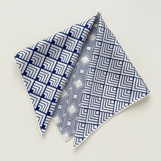Silk scarf with white background and blue geometric pattern featuring concentric squares and linear designs, folded to show different pattern angles.