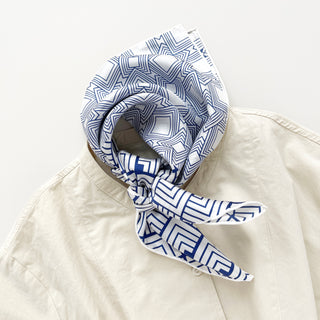 Silk scarf with white background and blue geometric pattern, styled in a knot around collar of cream garment, showing hand-rolled edges