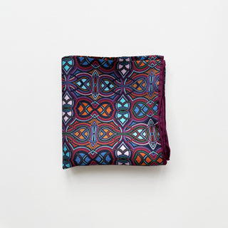 Folded silk men's neckerchief with vibrant abstract geometric pattern featuring plum purple, blue, orange and teal colors with hand-rolled edges