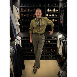 Man wearing retro geometric pattern silk neckerchief scarf with green khaki jacker style shirt – men’s square silk scarf, standing in a well-organised closet with shelves of shoes and clothing.
