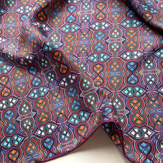 Plum purple silk neckerchief with intricate geometric pattern featuring blue, orange, and white interlocking designs with visible hand-rolled edge