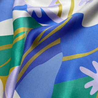 Luxurious silk scarf with abstract lotus pattern in vibrant blue, green, lilac, and mustard yellow, showing the smooth, shimmering fabric texture