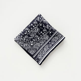 Square black silk scarf with white paisley pattern and detailed border, neatly folded to display intricate design on premium twill fabric